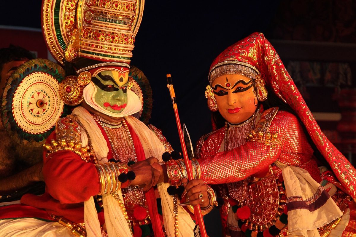 Two Kathakali performers in painted faces, headdresses and layered costume, mid-performance.