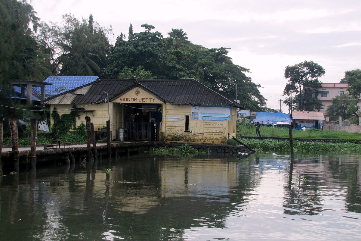 The Vaikom boat jetty seen across still water, with its tiled roof reflected below.