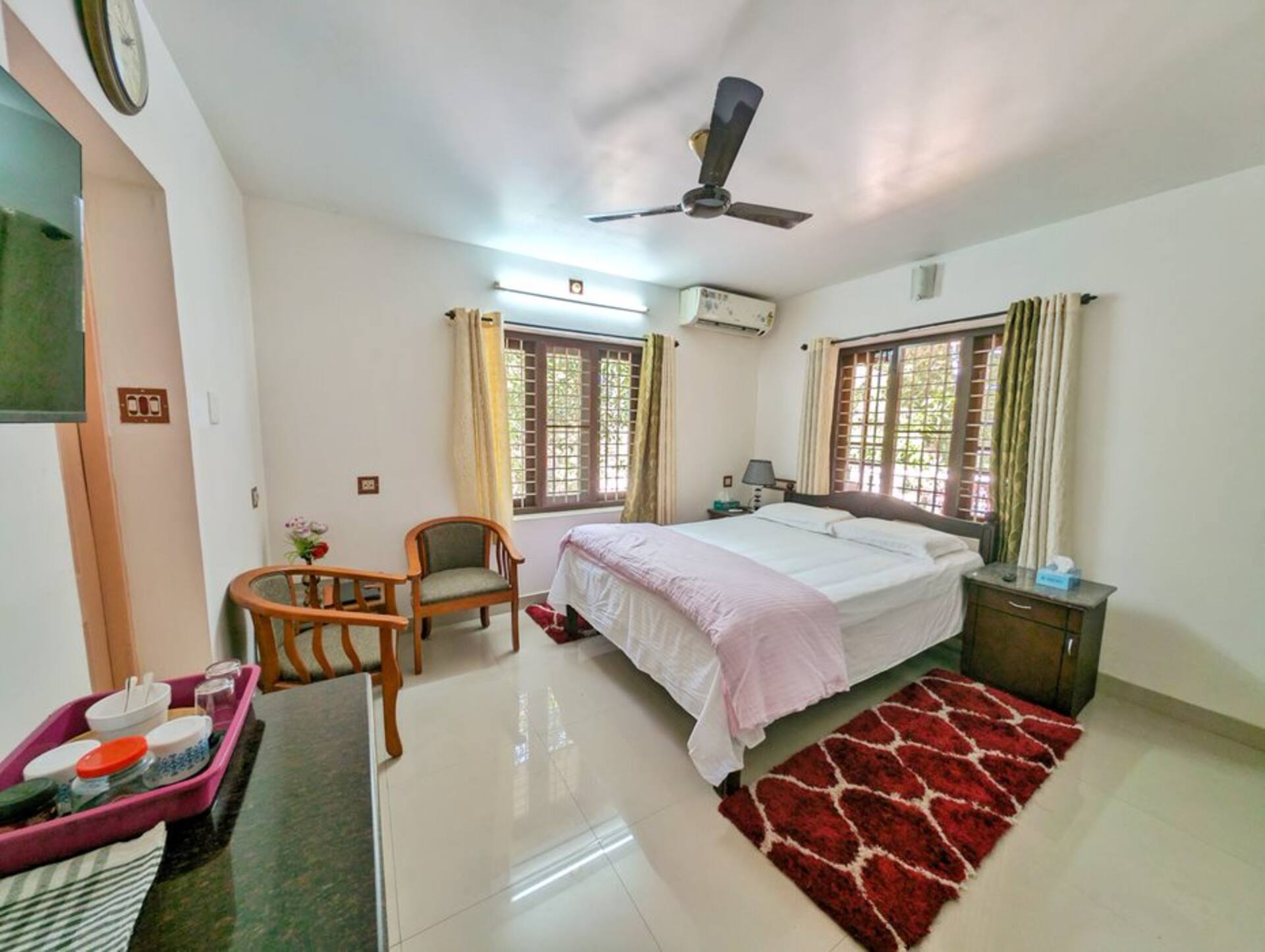 The Coral Room: a double bed with white linen, a coral-painted alcove, cane chairs and windows onto the garden.