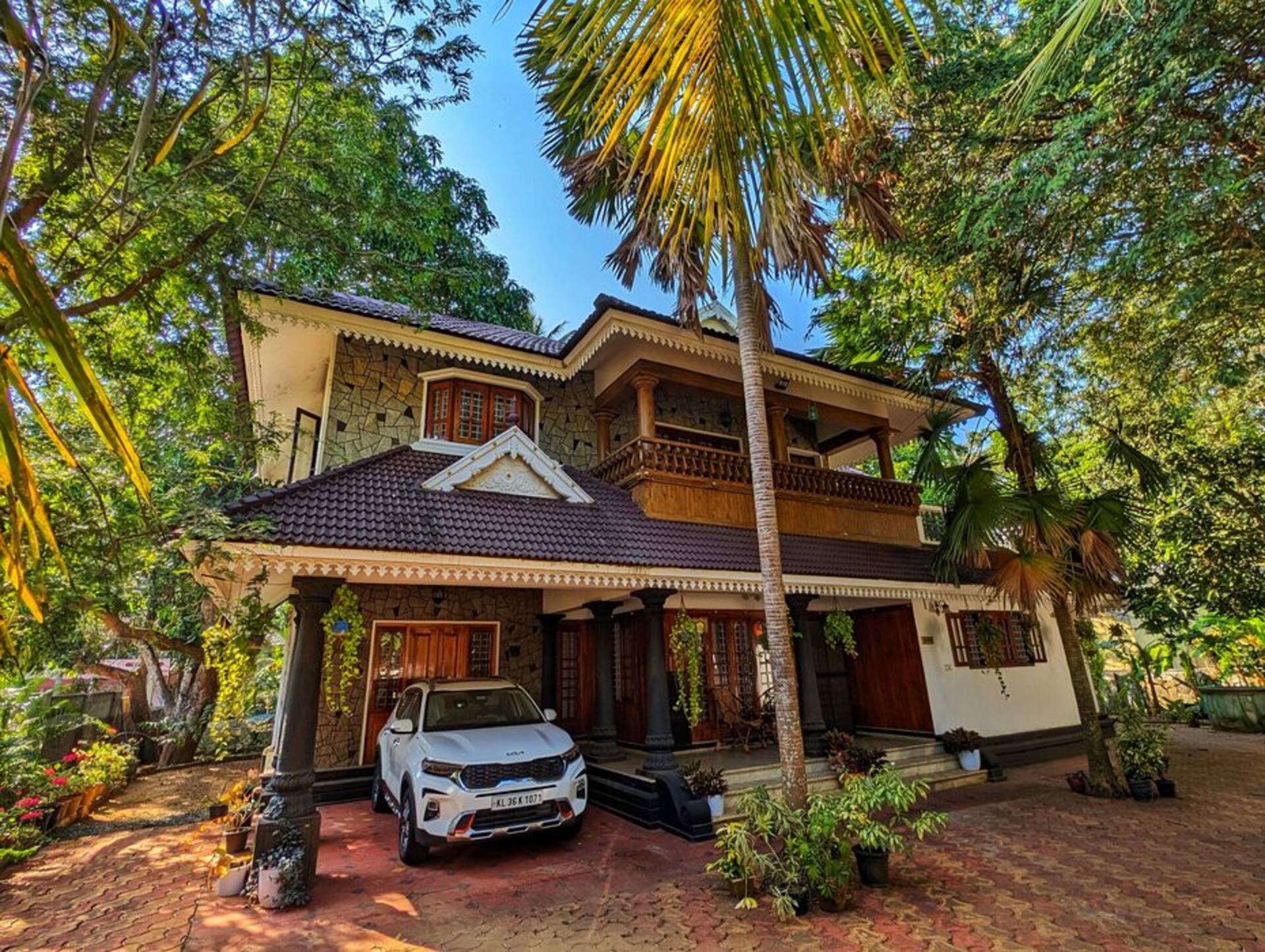 The front of Ushas Homestay: a tiled-roof Kerala house with carved stone pillars, framed by palms and mango trees.