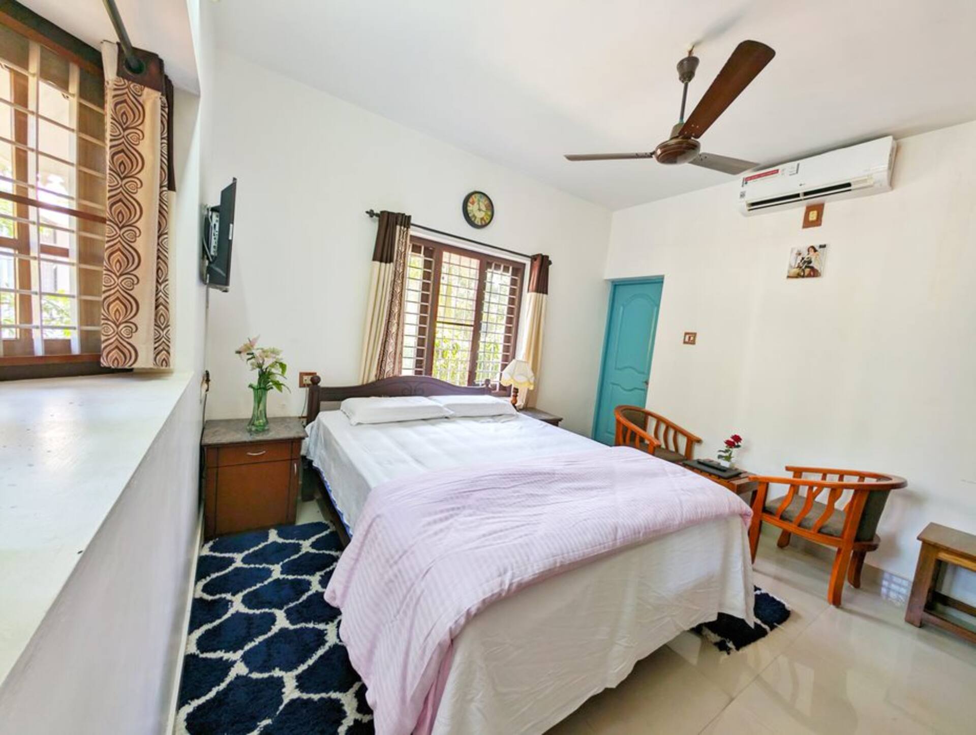 The Sapphire Room: a double bed, a teal-blue door to the bathroom, teak furniture and bright windows.