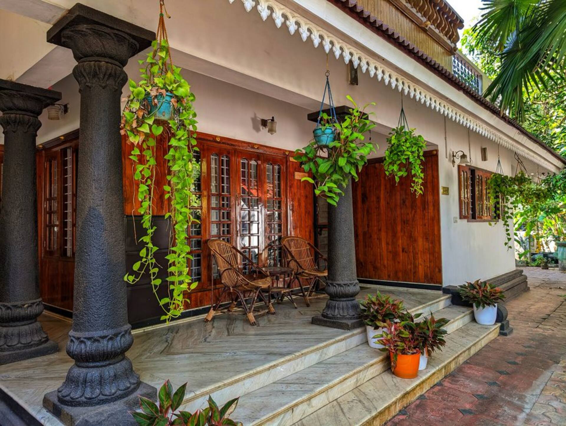 The covered sit-out with cane chairs, carved stone pillars and hanging money-plant baskets.